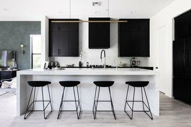 Šiuolaikinė virtuvė su juodomis spintelėmis, baltais stalviršiais ir juodomis išmatomis