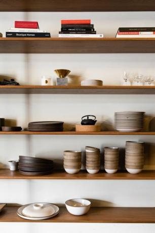 Houten planken met boeken, bruin en neutraal servies en een zwarte theepot.