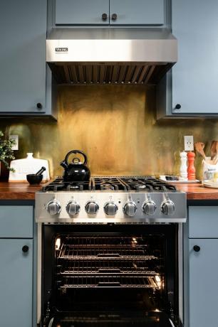 Backsplash de latão atrás do fogão na cozinha com armários pintados de azul.