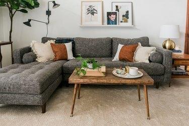 Midcentury-inspirerat soffbord i trä med dekorativ bok, krukväxt och tallrik med ljus på brun matta mot grå soffa i modernt vardagsrum