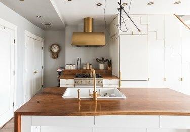 сиво-бяла кухня с дървен плот и качулка от месинг