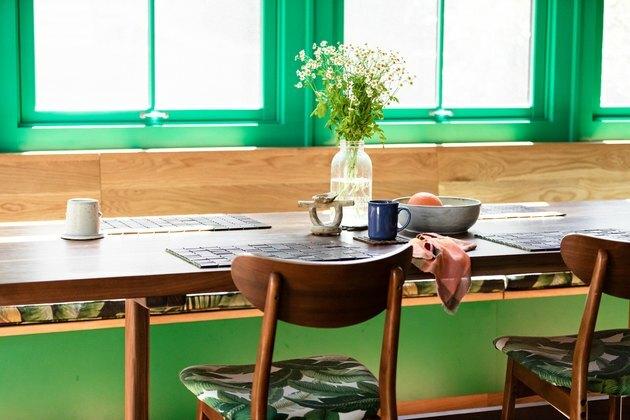 roheline aknakaunistus puidust hommikusöögilaua taga koos puittoolide ja lillega laual