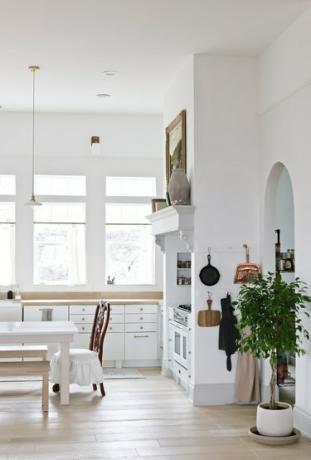 Cucina a vista con pareti in gesso bianco, una porta ad arco e pavimenti in legno.