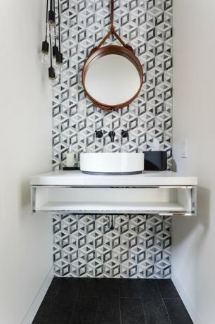 Badkamer onder trap met grijze en witte moderne backsplash en ronde spiegel