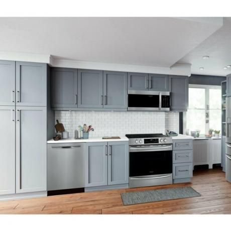 Fogão a gás em aço inoxidável com micro-ondas acima, armários cinza claro, lava-louças e backsplash de ladrilho branco do metrô.