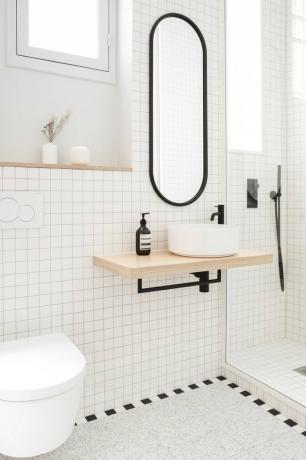 Banheiro branco com penteadeira moderna, pia redonda, torneira preta, espelho oval emoldurado preto, azulejos brancos e idéias escandinavas de armazenamento de banheiro.