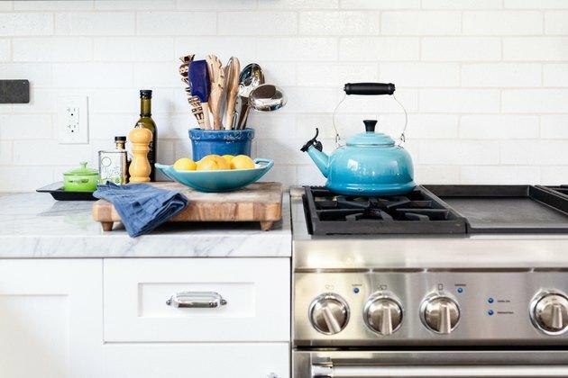 Fireclay azulejos brancos atrás do fogão na cozinha com chaleira azul.