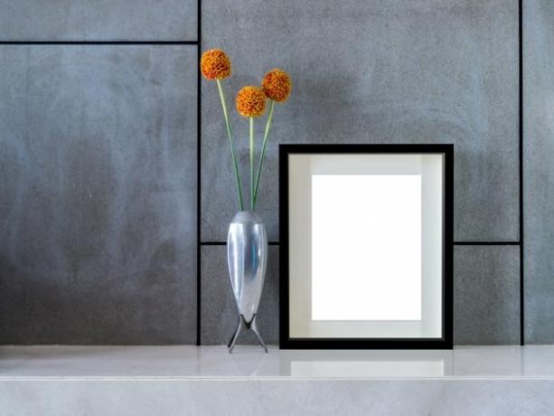 Moderne innervegg med blomstervase og blank bilderamme