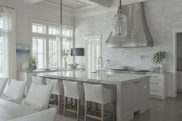 Hvitt kjøkken med rustfritt hette, kjøkkenøy, barkrakker.