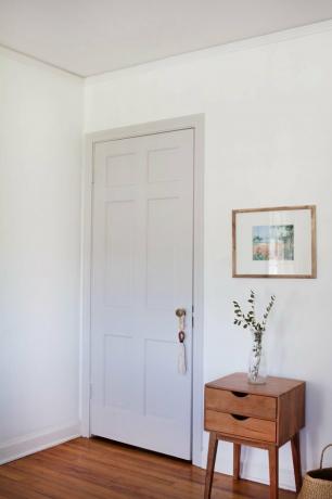 باب معجون مطلي باللون ، وجدران بيضاء ، وطاولة جانبية خشبية مع نبات.
