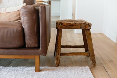 Un piccolo sgabello di legno accanto a un divano in pelle marrone.