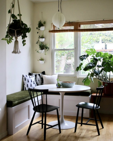 Keukenhoekidee met witte tulpentafel en zwarte bistrostoelen in een keukenhoekje met veel planten