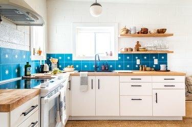 una cucina con armadi bianchi, pareti bianche e un backsplash fatto di grandi piastrelle azzurre ciascuna con una stella al centro