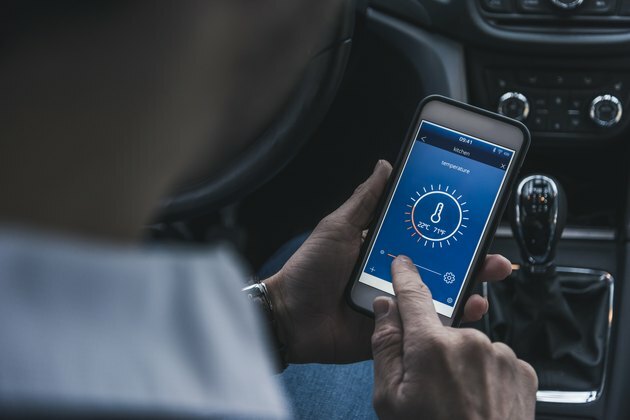 Човек в автомобил, който настройва умно устройство за дома чрез смартфон