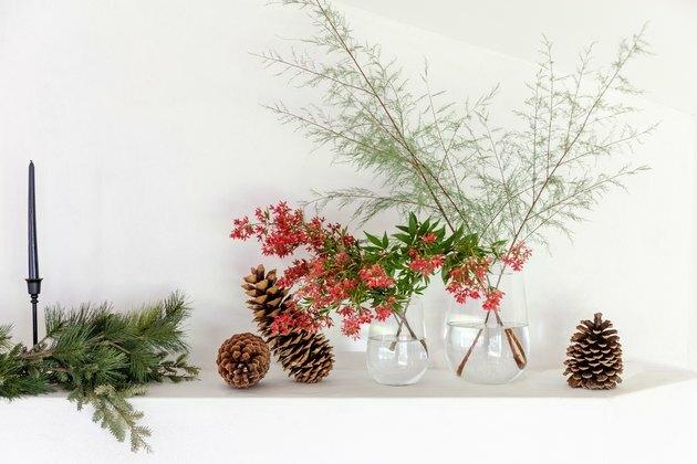 flores vermelhas frescas em vasos de vidro transparente sobre a lareira com pinhas e folhagem de inverno