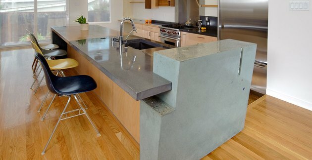 جزيرة خرسانية ثلاثية الألوان في مطبخ حديث بأرضيات خشبية وكراسي Eames