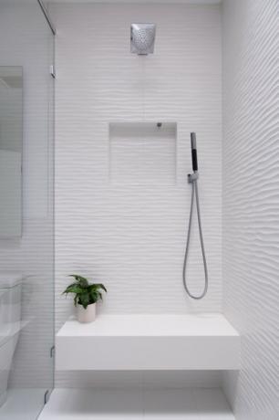 hvit dusj med benk som har et lite anlegg på, glassdør, dusjhode over hodet og håndholdt dusjhode