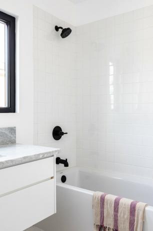 Banheiro moderno com banheira branca com torneira preta, toalha branca e roxa pendurada na banheira e bancada de mármore