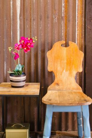 Uma cadeira de madeira vintage com pernas azuis ao lado de uma mesa lateral com orquídeas cor de rosa