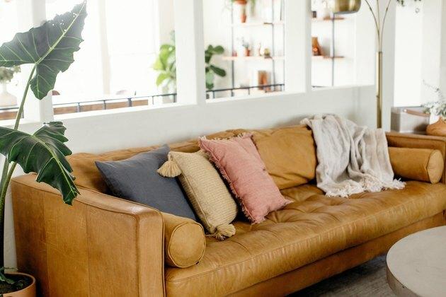 Ruda odinė sofa su neutraliomis mesti pagalvėmis