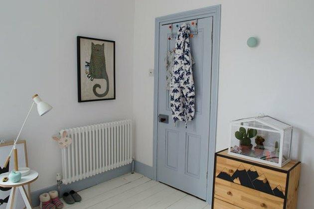 Minimalistische kinderslaapkamer met blauwe deur en kattenkunst aan de muur