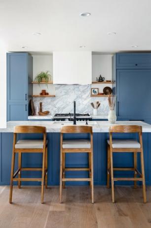 Et kjøkken med blå skap og trebarstoler på en kjøkkenøy