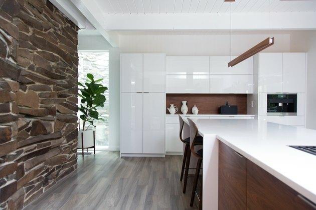 cucina a vista con muro in pietra, mobili bianchi, isola cucina effetto legno