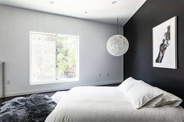 חדר שינה מינימליסטי עם קיר מבטא שחור, מנורת תליון גלובוס מחרוזת, שטיח פרווה אפור ואומנות צילום
