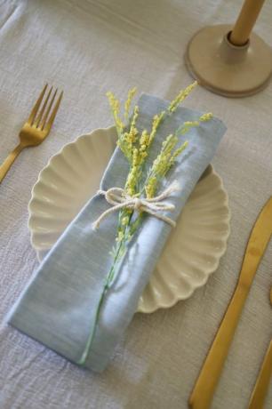 Servilleta de cambray azul en un plato con flores amarillas atadas en la parte superior