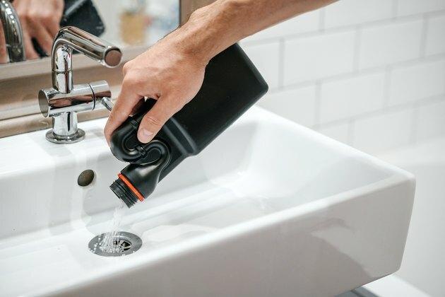 Odstranitev blokade v umivalniku, roki človeka s steklenico posebnega zdravila z zrncmi.