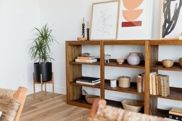 Como organizar uma estante de livros uma estante de madeira com livros e outras bugigangas decorativas ao lado de uma planta em um vaso preto.