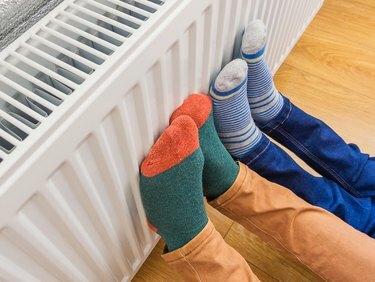 Donna e bambino che indossano un paio di calzini di lana colorati che riscaldano i piedi freddi davanti al radiatore di riscaldamento in inverno. Stufa elettrica o a gas a casa.