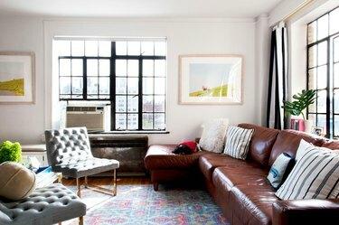 en stue domineres av to grå polstrede stoler, et fargerikt pastellteppe og en skinnsofa