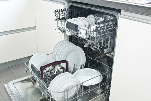 Åben opvaskemaskine med rene tallerkener i det hvide køkken