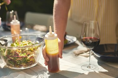 شخص يحمل زجاجة ضغط على الطاولة بالقرب من وعاء السلطة وزجاج النبيذ