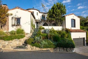 exteriör av hemmet i spansk stil med frodig landskapsarkitektur och stödmurar av sten