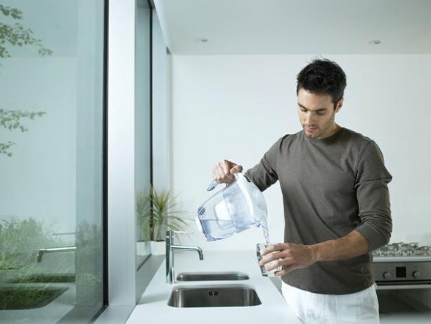 Man i kök som häller exponeringsglas av filtrerat vatten