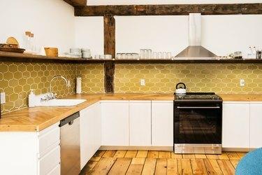 et køkken med åbne hylder, brede plankede trægulve og en bagplade af høstguldfliser