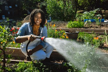 La fondatrice di Loam Candles, Jessica White, una donna con i capelli corti e neri, innaffia un'aiuola in un orto comunitario.