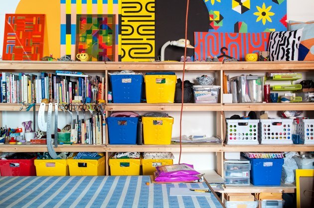 Organização do ensino doméstico com caixas amarelas, vermelhas e azuis nas prateleiras com materiais de arte, livros, arte.