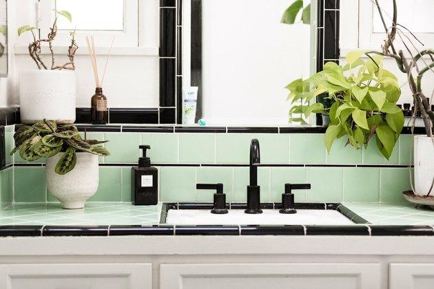 forfengelighet på badet med hvite skap, grønne og sorte keramiske fliser, hvite planter med grønne planter