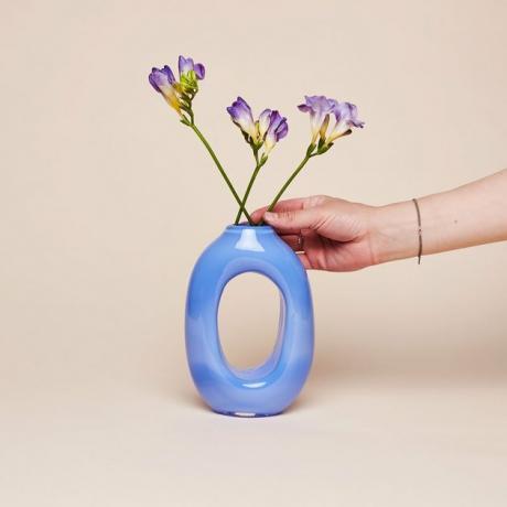 vaso azul com mão colocando flores roxas dentro