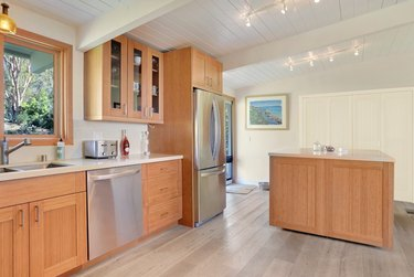 Cozinha com armários de bambu, trilhos de iluminação, piso de madeira, eletrodomésticos inox.