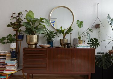 midcentuy credenza in woonkamer met boho planten en ronde gouden spiegel