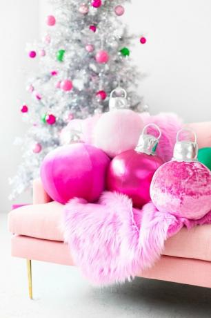 „Pasidaryk pats“ kalėdinės dekoracijos su rausvų pagalvių ornamentais ant rožinės sofos