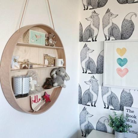 Organização do quarto infantil com prateleira suspensa circular e papel de parede preto e branco de raposa