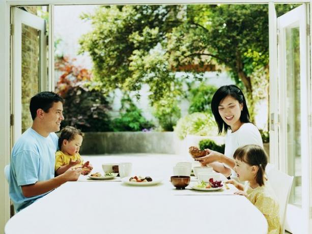 Семейство от четирима вечери на маса с френски прозорци, отворени към двор