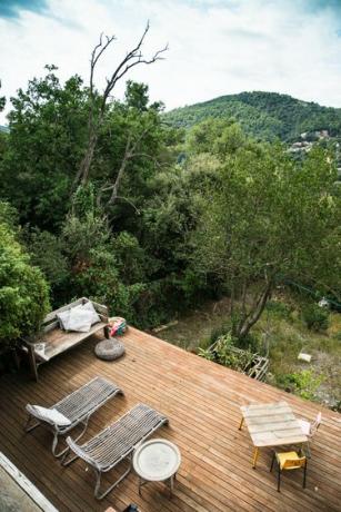 Een houten terras met uitzicht op bergen en bomen met een tuinmeubelset