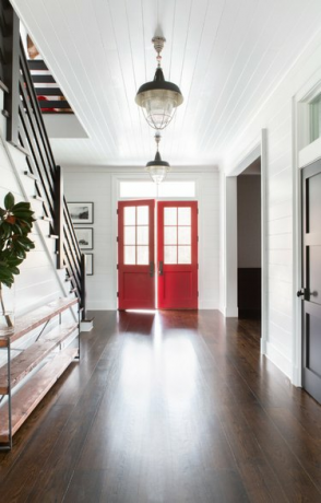 Luz suspensa de corredor na entrada com portas vermelhas, luzes suspensas, piso de madeira, escadas, aparador.