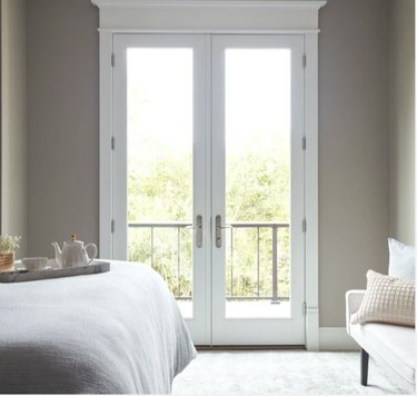 Imagen de puertas de patio mirando desde un dormitorio. La habitación tiene una cama con ropa de cama blanca con una bandeja de desayuno y un sofá blanco contra la pared.